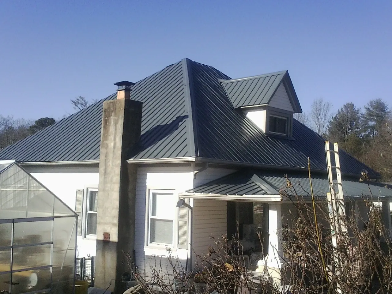 Dark blue standing seam metal roof on a white farmhouse with dormer — Slate & Tile Roof Repair by Roofing Brothers in Iron Gate