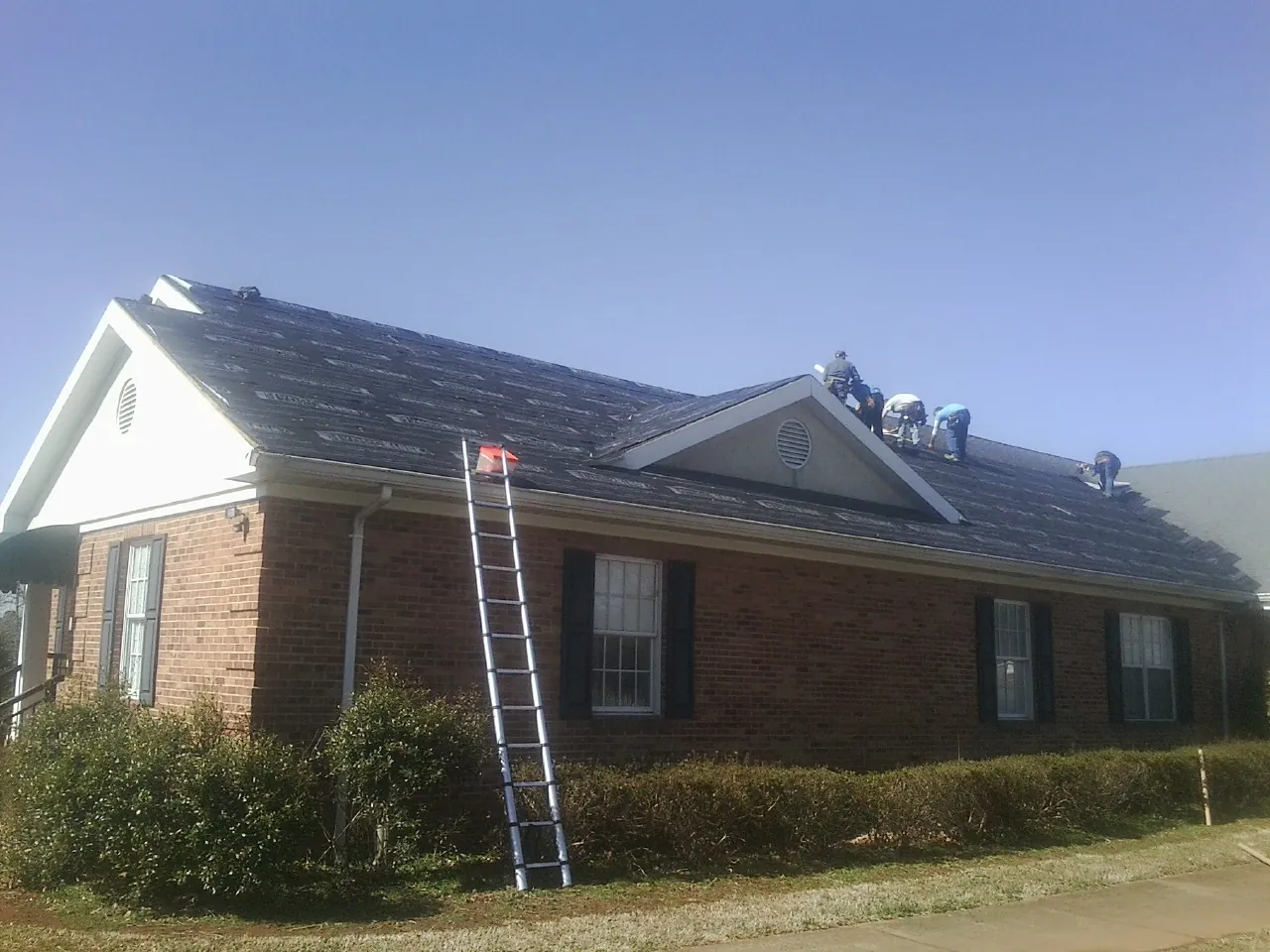 Crew tearing shingles off a brick ranch roof with a ladder set — Metal Roof Repair work by our crew in Iron Gate