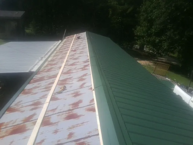 Old rusted panels beside newly installed green metal roofing — Wind Damage Roof Repair by Roofing Brothers in Iron Gate