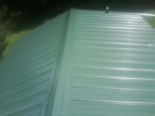 New green metal panels meeting at the ridge of a roof — Flat Roof Repair work by our crew in Iron Gate