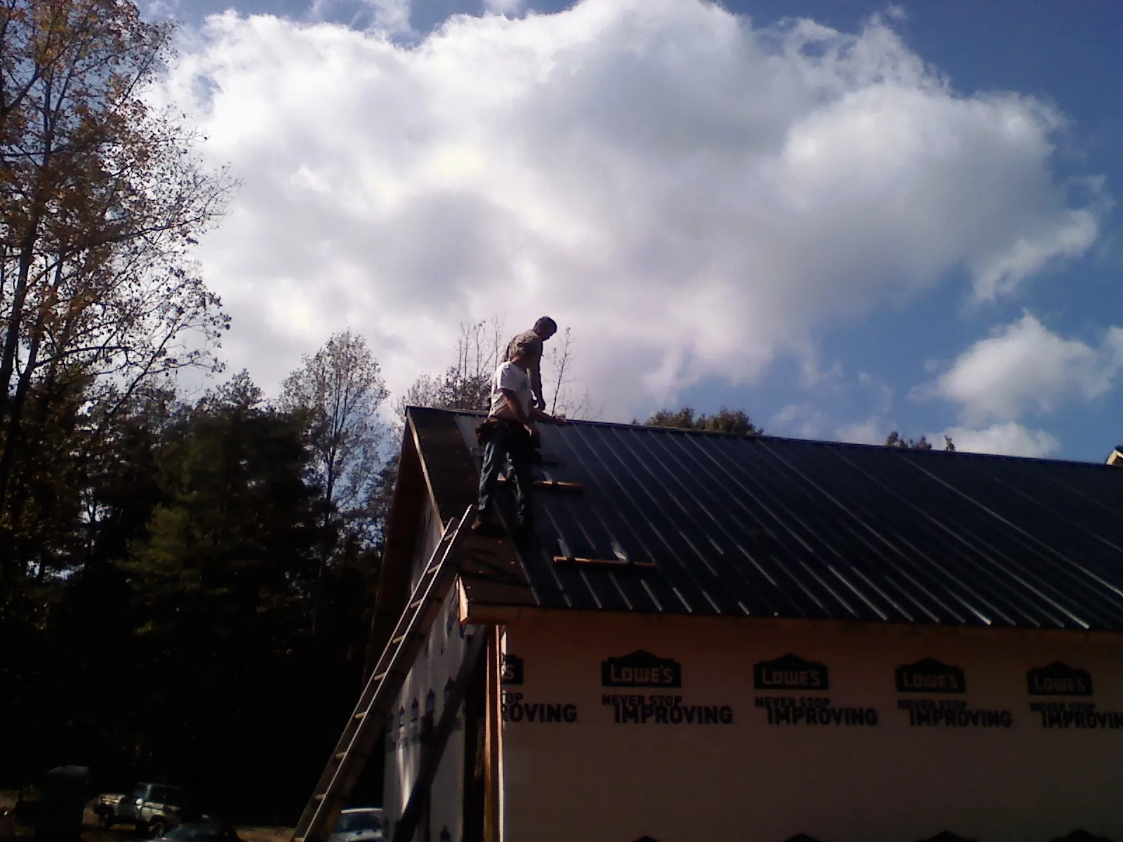 Roofer fastening dark metal panels high against a cloudy sky, from a Roof Inspection job in Iron Gate