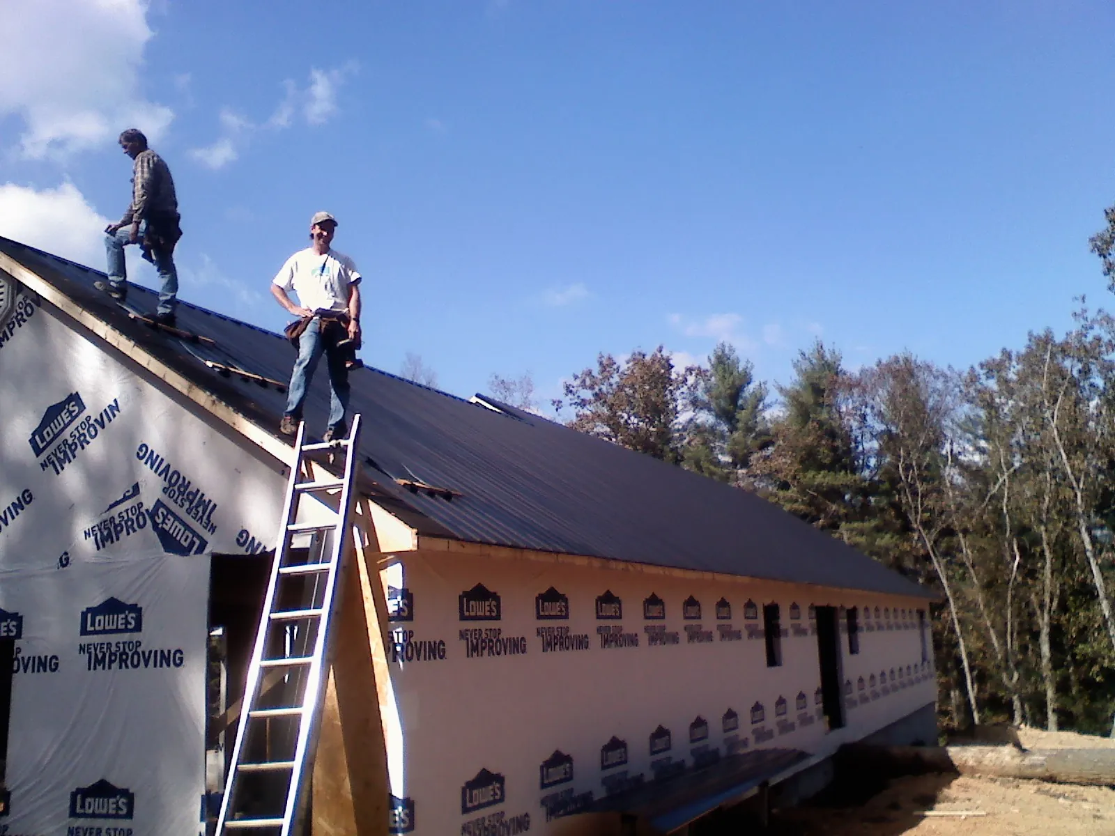 Two roofers standing on a long dark metal roof over a wrapped building in Iron Gate