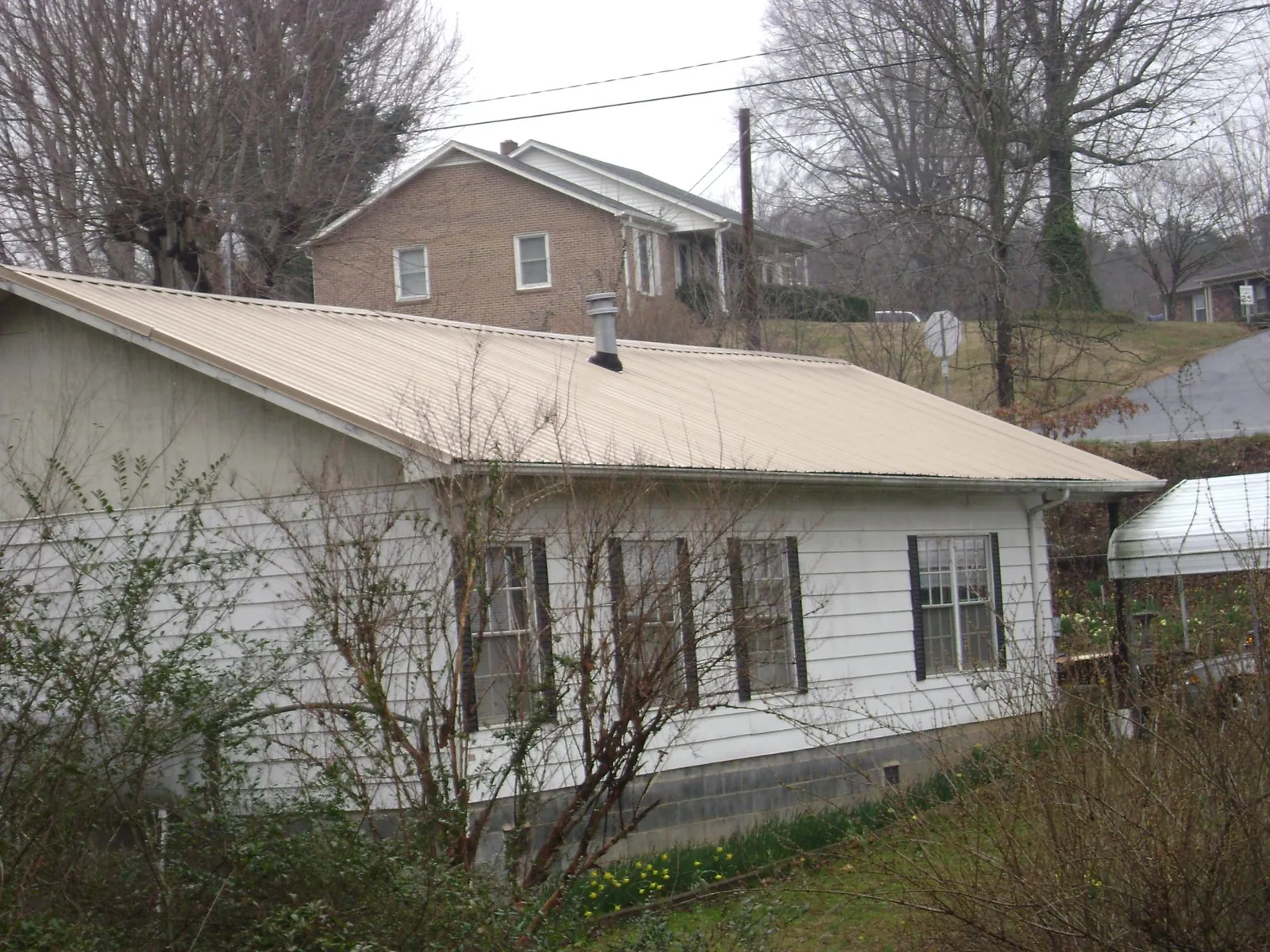 Tan metal roof on a white sided house set into a hillside — Commercial Roofing by Roofing Brothers in Iron Gate